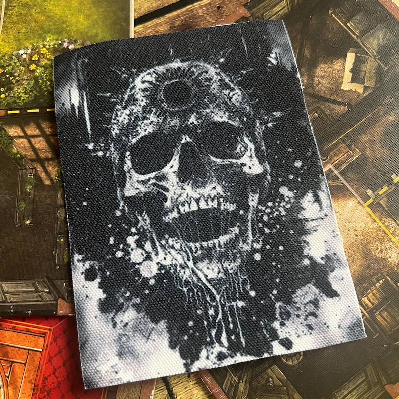May include: A black and white skull with a third eye on its forehead, surrounded by white paint splatters on a black background.
