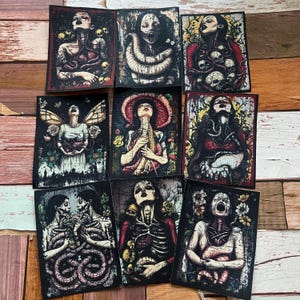 May include: Nine rectangular art prints with gothic and surreal illustrations. The prints depict figures with exposed anatomy, snakes, and floral elements, in dark, muted colours with red and yellow accents. The artwork has a vintage, macabre aesthetic.