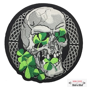 Könnte beinhalten: Ein gestickter Schädel in Schwarzweiß mit grünen Kleeblättern in seinen Augen und seinem Mund. Der Schädel ist von einem silbernen keltischen Knotendesign umgeben. Der Patch ist 22,5 cm x 22,5 cm groß.