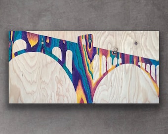 Può includere: Un pannello di legno con una silhouette di un ponte color arcobaleno. Il ponte ha archi e una torre. La venatura del legno è visibile sullo sfondo.