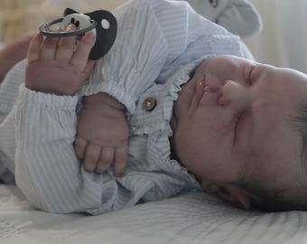May include: A sleeping baby doll wearing a blue and white striped onesie with a pacifier in its mouth.