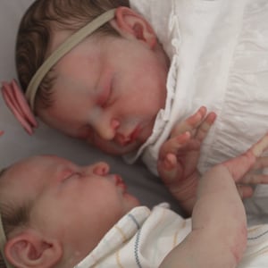 Op de afbeelding: Twee slapende babypoppen met hoofdbanden met strikjes. De ene pop draagt een witte jurk en de andere een gestreept shirt.