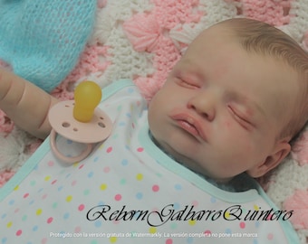 May include: A sleeping reborn baby doll wearing a light blue and white polka dot onesie with a pink pacifier. The doll is lying on a pink and white crocheted blanket.