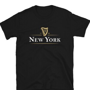 May include: Black t-shirt featuring a gold harp logo with the text "NEW YORK" underneath. The harp has the numbers "17" and "59" on either side.