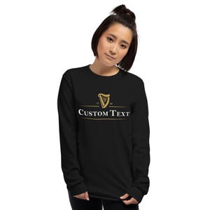 K&ouml;nnte beinhalten: Schwarzes Langarmshirt mit einem goldenen Harfenlogo und dem Text "CUSTOM TEXT" auf der Vorderseite.