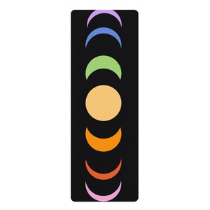 May include: Black yoga mat featuring a colorful design of crescent moons and a sun. The moons are in shades of purple, blue, green, orange, and pink, with a yellow sun in the center. The mat is rectangular and designed for exercise.