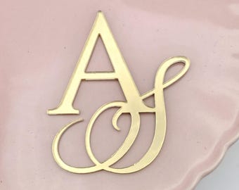 May include: Gold-colored metal monogram with the letters "A" and "S" intertwined. The "A" is a simple block letter, while the "S" is a stylized script letter.