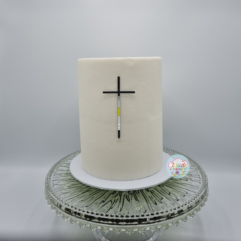 A mirror silver acrylic crucifix charm stuck to the front of a cake