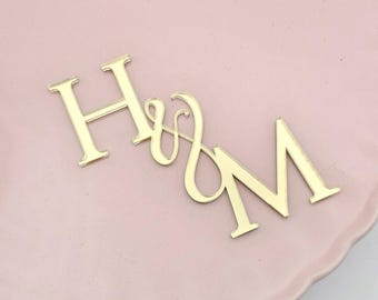 May include: Gold-colored metal letters spelling "H & M" on a pink background.