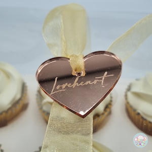 May include: Rose gold heart-shaped acrylic tag with the word "Loveheart" written in cursive. The tag is tied to a white satin ribbon.