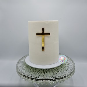 A mirror gold acrylic crucifix charm stuck to the front of a cake