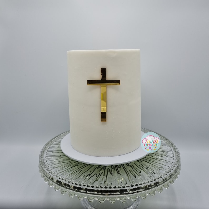 A mirror gold acrylic crucifix charm stuck to the front of a cake