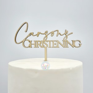 Wooden name topper with a spike stuck into the top of a cake. The topper has the name in a script font with "CHRISTENING" written in a block font underneath.