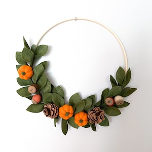 Peut inclure: Une couronne d'automne faite à la main avec un cerceau en bois orné de feuilles en feutre, de citrouilles oranges, de pommes de pin et de glands. Une décoration pour la saison automnale, sur fond neutre.