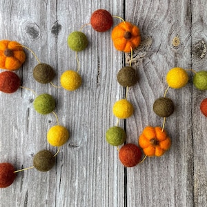May include: A fall-themed garland featuring felt pumpkins and round balls in shades of orange, yellow, green, and brown. The garland is strung on a thin, gold-colored thread, perfect for autumn decor. The pumpkins are approximately 2 inches in diameter.