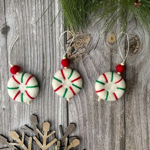 Puede incluir: Tres adornos navide&ntilde;os hechos a mano. Cada adorno es blanco con rayas rojas y verdes, una cuenta roja y una cuerda blanca para colgar. Los adornos son redondos y tienen un dise&ntilde;o de caramelo de menta.