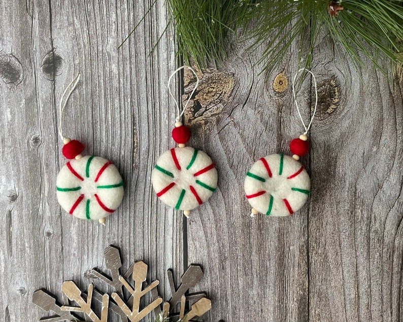 Puede incluir: Tres adornos navide&ntilde;os hechos a mano. Cada adorno es blanco con rayas rojas y verdes, una cuenta roja y una cuerda blanca para colgar. Los adornos son redondos y tienen un dise&ntilde;o de caramelo de menta.