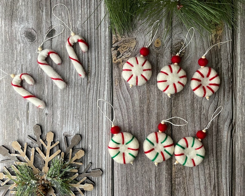Puede incluir: Una colecci&oacute;n de adornos navide&ntilde;os hechos a mano. Los adornos incluyen bastones de caramelo con rayas rojas y adornos redondos con rayas rojas y verdes. Cada adorno tiene una cuerda para colgar y una cuenta roja.