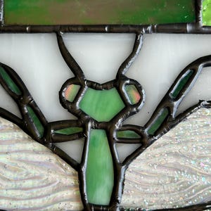 Pu&ograve; includere: Un pannello in vetro colorato con un design stilizzato di insetto. L'opera d'arte utilizza vetro verde, bianco e iridescente, incorniciato con metallo scuro. Il corpo dell'insetto &egrave; di un verde vibrante, con ali e antenne dettagliate.