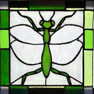 Pu&ograve; includere: Pannello in vetro colorato raffigurante una mantide religiosa verde con ali bianche, contornata di nero. L'insetto &egrave; centrato all'interno di un quadrato di vetro trasparente e verde, incorniciato da un bordo di vetro verde e nero.