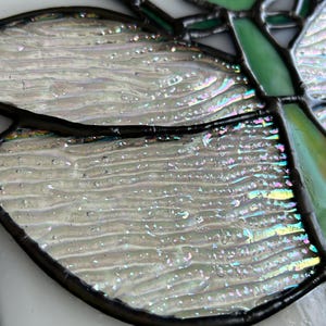 Pu&ograve; includere: Primo piano di una vetrata a forma di farfalla con ali iridescenti. Le ali sono di un bianco perlaceo con sottili sfumature arcobaleno. Il corpo e i contorni della farfalla sono neri e le antenne sono verdi.