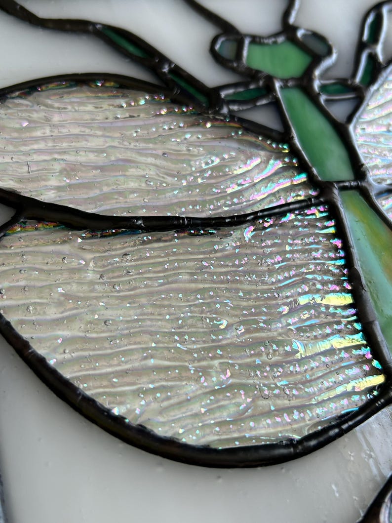 Pu&ograve; includere: Primo piano di una vetrata a forma di farfalla con ali iridescenti. Le ali sono di un bianco perlaceo con sottili sfumature arcobaleno. Il corpo e i contorni della farfalla sono neri e le antenne sono verdi.