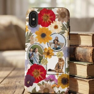 May include: A phone case featuring a collage of pressed flowers in red, yellow, purple, and white. The case includes framed photos of people and a cat. The background is white with a wood grain texture.