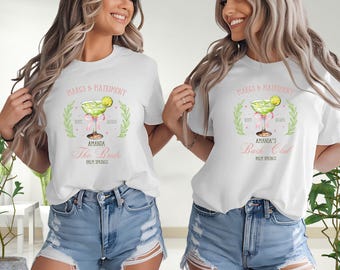 Puede incluir: Dos camisetas blancas con un diseño de margarita y texto. Una dice "Margs & Matrimony" y "Amanda The Bride Palm Springs". La otra dice "Amanda's Bach Club Palm Springs". Ambas tienen una ilustración de margarita verde.