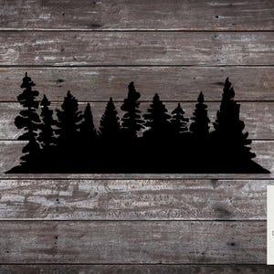 May include: Black silhouette of a forest with pine trees against a woodgrain background. The image includes the text "Decal Vinyl Workz" in white letters.