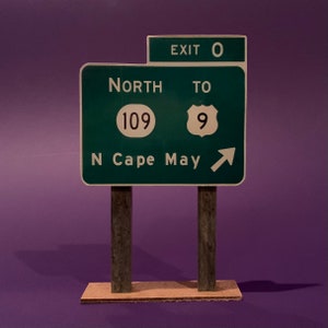 May include: Green road sign with white text and numbers. The sign reads "EXIT 0 NORTH TO 109 9 N Cape May" with an arrow pointing to the right.