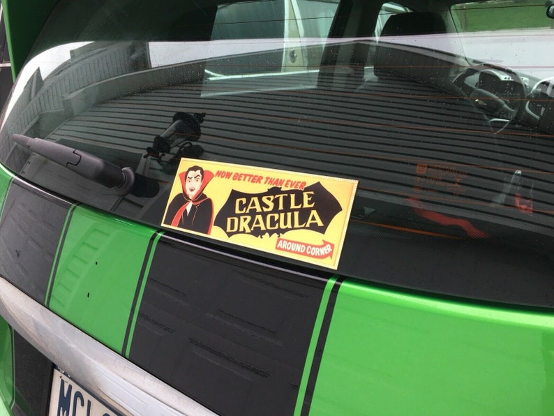 May include: A green car with black racing stripes and a sticker that says "Now Better Than Ever Castle Dracula Around The Corner".