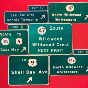 May include: A collection of green and white highway signs with arrows pointing in different directions. The signs include exit numbers, road names, and destinations such as Sea Isle City, Wildwood, and North Wildwood.
