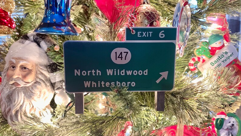 May include: A green and white highway sign with the text "North Wildwood Whitesboro" and a white circle with the number "147" inside. The sign also has a white arrow pointing to the right. Above the sign is a smaller green sign with the text "EXIT 6".