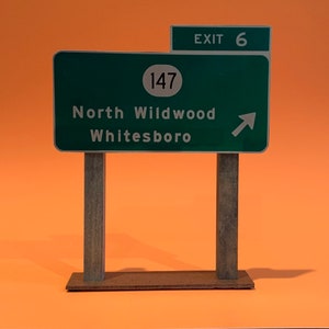 May include: A green road sign with white text and a white arrow pointing to the right. The sign reads "Exit 6", "147", "North Wildwood", and "Whitesboro".
