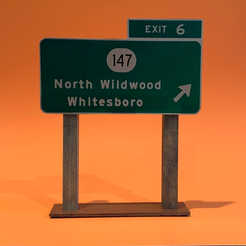 May include: A green road sign with white text and a white arrow pointing to the right. The sign reads "Exit 6", "147", "North Wildwood", and "Whitesboro".