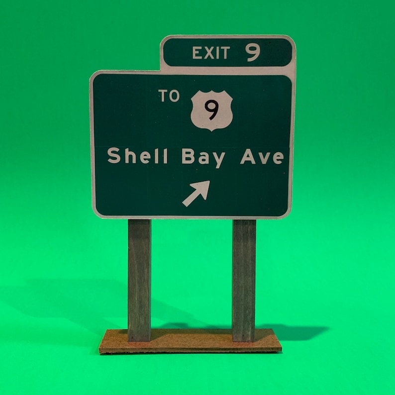 May include: Green highway sign with white text and a white arrow pointing to the right. The sign reads "Exit 9 To Shell Bay Ave".
