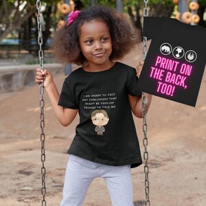 May include: Black t-shirt with a white graphic of a cartoon character with the text "I am ready to face any challenges that might be foolish enough to face me". The back of the shirt has the text "PRINT ON THE BACK, TOO!" in pink.