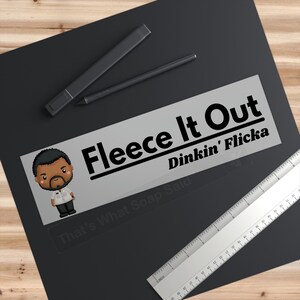 May include: A grey and white sticker with the text "Fleece It Out" and "Dinkin' Flicka" in black. Below the text is a cartoon illustration of a man with a moustache and a black and white striped shirt. The text "That's What Soap Said" is below the illustration.