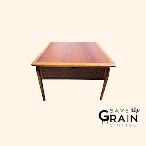 May include: A mid-century modern end table with a woven wicker drawer and a wood top. The table has a light wood finish and is in good condition.