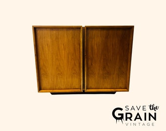 May include: A mid-century modern cabinet with two wooden doors. The cabinet is made of wood with a rich brown finish. The doors are closed and have a simple design.