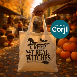 Puede incluir: Un bolso tote de color crema con gráficos negros, que incluyen un sombrero de bruja, murciélagos y la frase "Creep It Real Witches". El bolso se muestra frente a un fondo borroso de calabazas y follaje otoñal, ideal para Halloween.