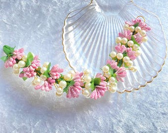 May include: A pink and white flower garland with pearl accents, displayed on a clear seashell-shaped dish.
