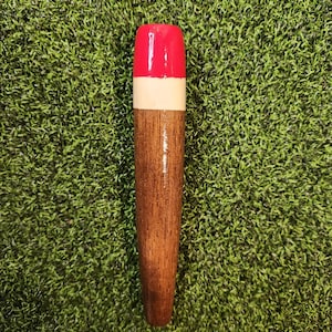 May include: A wooden bottle stopper with a red and white top. The stopper is brown and has a smooth finish.