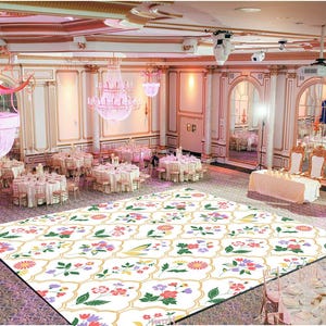 May include: A large, white dance floor with a colorful floral pattern. The dance floor is in a large, white room with white tables and chairs set up around the perimeter. There are chandeliers hanging from the ceiling.