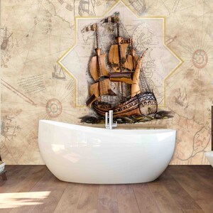 May include: A white bathtub sits in front of a bathroom wall with a vintage nautical map wallpaper featuring a brown sailing ship. The bathroom has a wooden floor and a brown wooden cabinet with a white toilet.