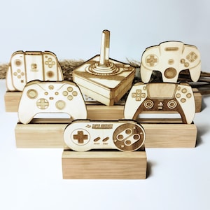 Peut inclure: Support en bois avec cinq manettes de jeux vidéo différentes, dont une Super Nintendo, une Playstation, une Xbox, une Nintendo 64 et une Sega Genesis. Chaque manette est sur un socle en bois séparé.