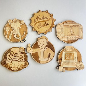 以下が含まれることがあります： Falloutをテーマにしたデザインのウッドコースター6枚セット。コースターには、Nuka Colaのロゴ、Pip-Boy、いいねをするVault Boy、パワーアーマーのヘルメット、そして2種類のPip-Boyの画面が描かれています。