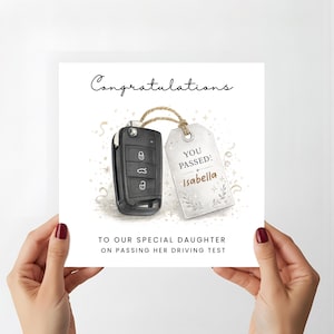 May include: A square greeting card featuring a black car key fob attached to a white gift tag with twine. The tag reads YOU PASSED! Isabella. The card text says Congratulations TO OUR SPECIAL DAUGHTER ON PASSING HER DRIVING TEST with gold stars.