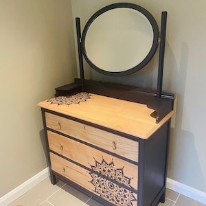 May include: A black vanity with three drawers and a round mirror. The drawers are painted black with a wood grain finish. The vanity has a mandala design painted on the front. The text "SOLD!" is in red letters at the bottom of the image.