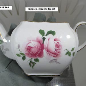 May include: White, lidless decorative teapot with a gold trim and a handle. The teapot is decorated with two pink roses and green leaves. The text "PITCHER09" and "lidless decorative teapot" are visible.